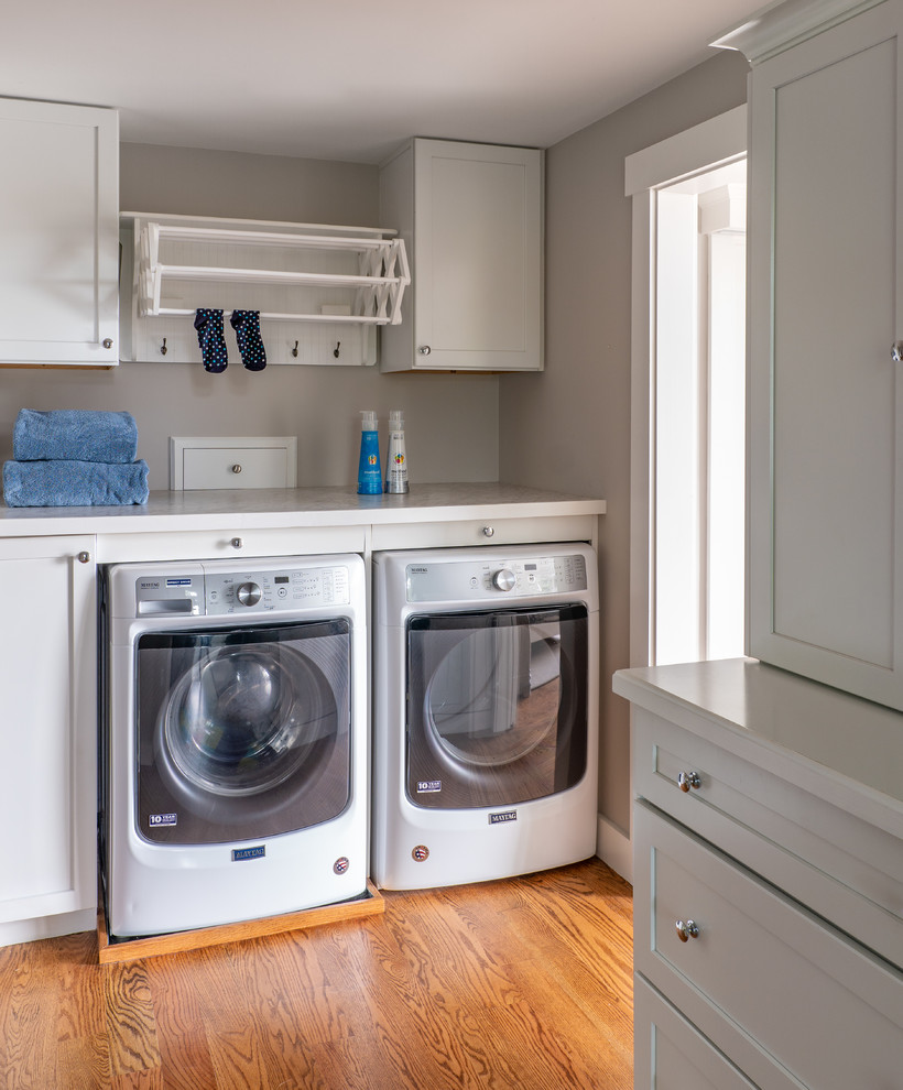 Photo of a mid-sized transitional single-wall dedicated laundry room in Boston with flat-panel cabinets, grey cabinets, grey walls, medium hardwood floors, a side-by-side washer and dryer, brown floor, white benchtop and laminate benchtops.
