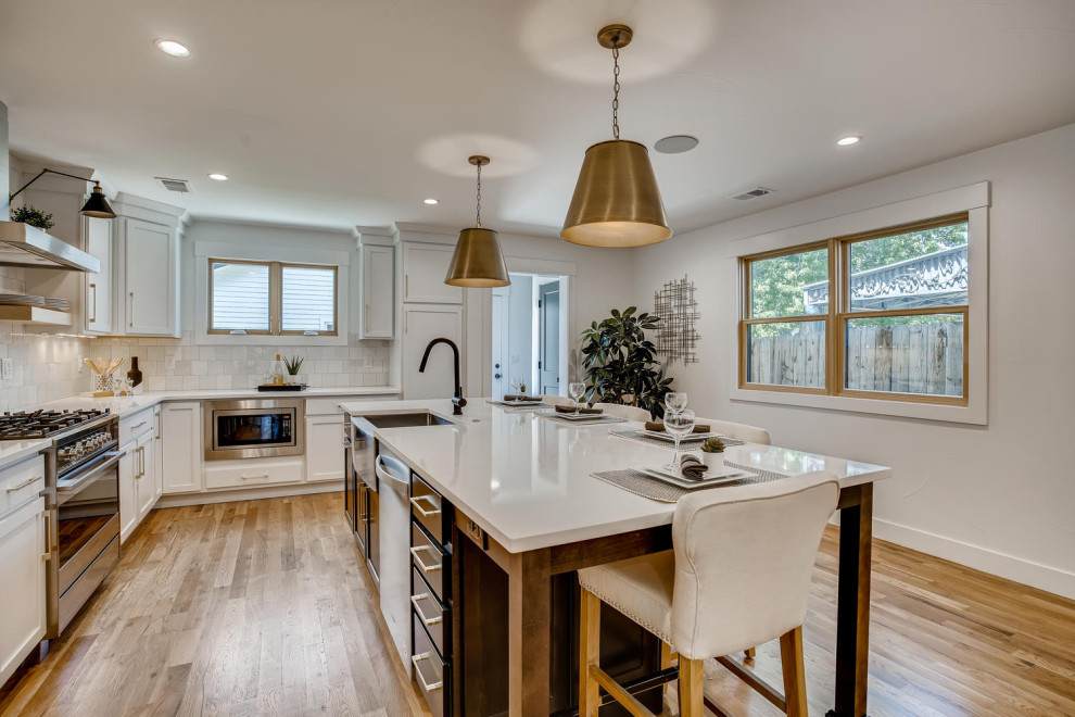 Mid-sized transitional l-shaped eat-in kitchen photo in Denver with a farmhouse sink, shaker cabinets, white cabinets, quartzite countertops, white backsplash, porcelain backsplash, stainless steel appliances and an island