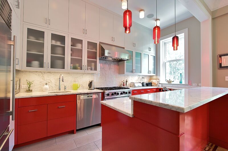 This is an example of a mid-sized eclectic l-shaped eat-in kitchen in New York with an undermount sink, flat-panel cabinets, red cabinets, marble benchtops, white splashback, stone slab splashback, stainless steel appliances, ceramic floors and with island.
