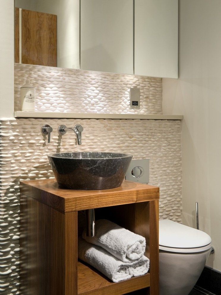 Design ideas for a mid-sized modern 3/4 bathroom in New York with flat-panel cabinets, dark wood cabinets, a wall-mount toilet, beige tile, pebble tile, beige walls, porcelain floors, a vessel sink, wood benchtops, grey floor and brown benchtops.