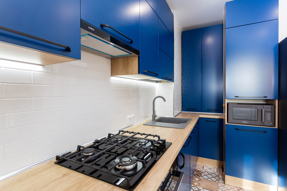 Идея дизайна: кухня среднего размера в современном стиле с плоскими фасадами, синими фасадами, белым фартуком, фартуком из керамической плитки и коричневой столешницей