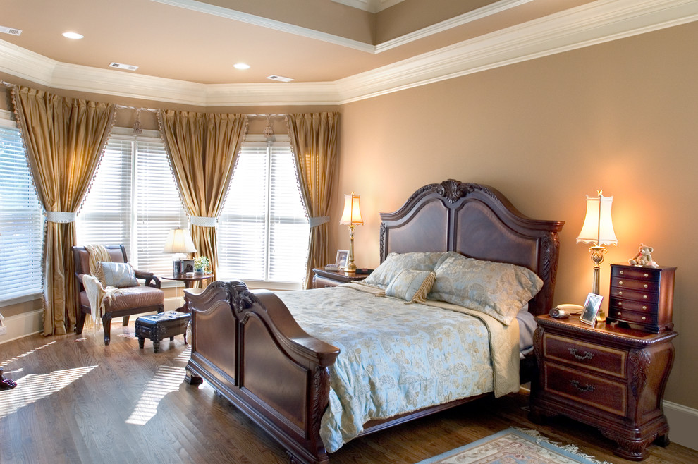 This is an example of a large country master bedroom in Atlanta with beige walls, dark hardwood floors and a stone fireplace surround.