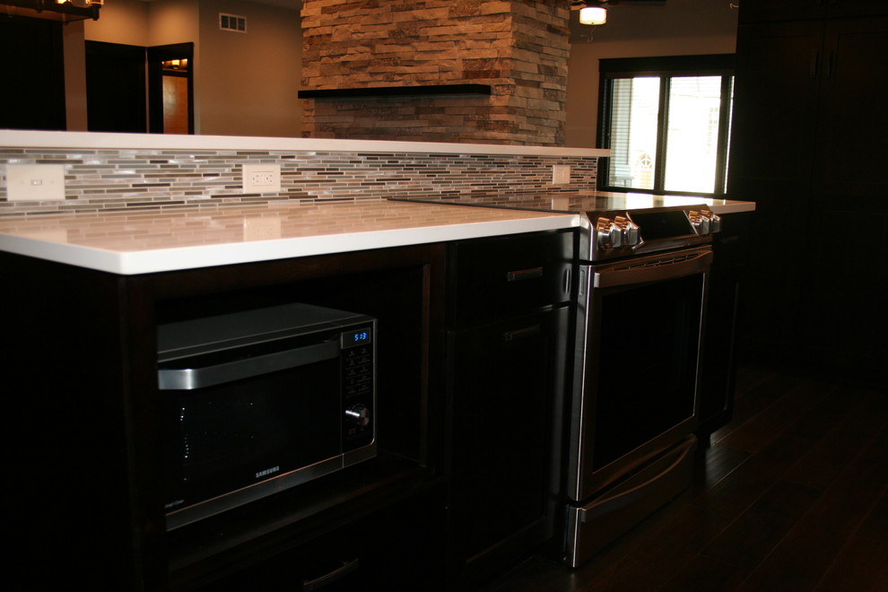 Inspiration for a mid-sized transitional l-shaped dark wood floor and brown floor open concept kitchen remodel with stainless steel appliances, an island, an undermount sink, shaker cabinets, black cabinets, quartz countertops, beige backsplash and porcelain backsplash