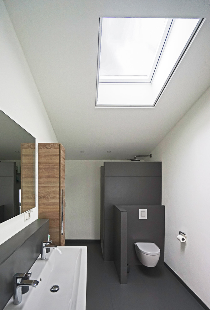 Inspiration for a mid-sized contemporary 3/4 bathroom in Cologne with medium wood cabinets, an open shower, a wall-mount toilet, gray tile, white walls, a trough sink and an open shower.