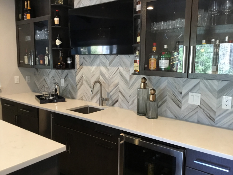 Large modern l-shaped seated home bar in New York with an undermount sink, flat-panel cabinets, dark wood cabinets, quartz benchtops, grey splashback, marble splashback, painted wood floors, grey floor and white benchtop.