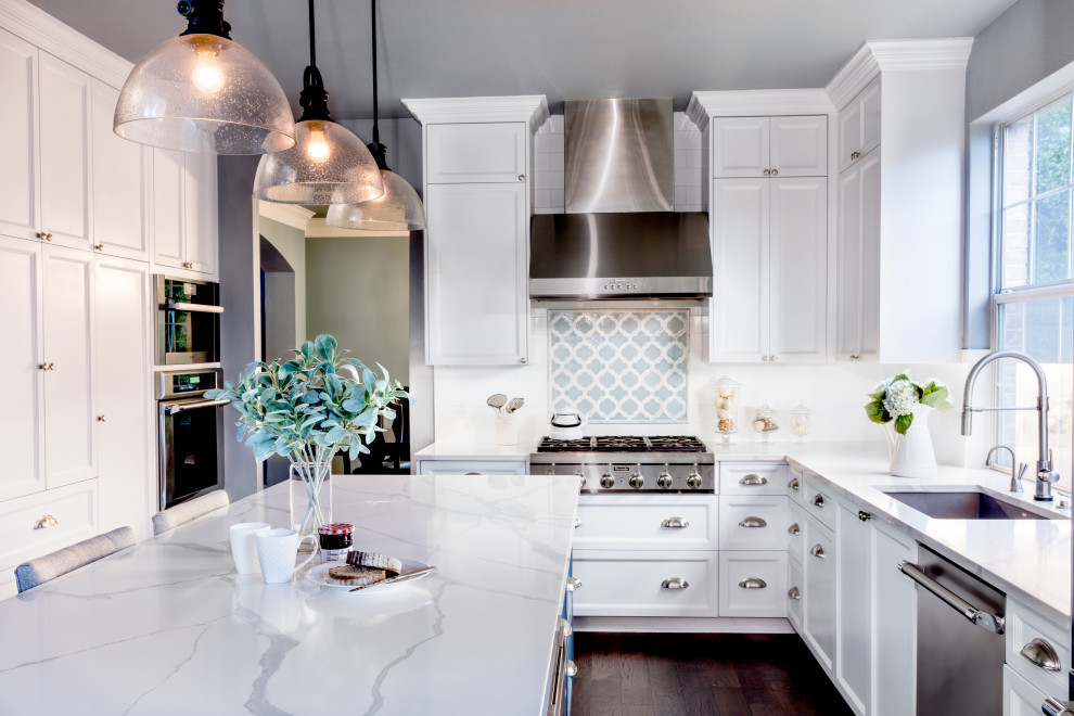 Inspiration for a mid-sized traditional l-shaped eat-in kitchen in Austin with a single-bowl sink, shaker cabinets, white cabinets, quartz benchtops, white splashback, ceramic splashback, stainless steel appliances, dark hardwood floors, with island, brown floor and white benchtop.