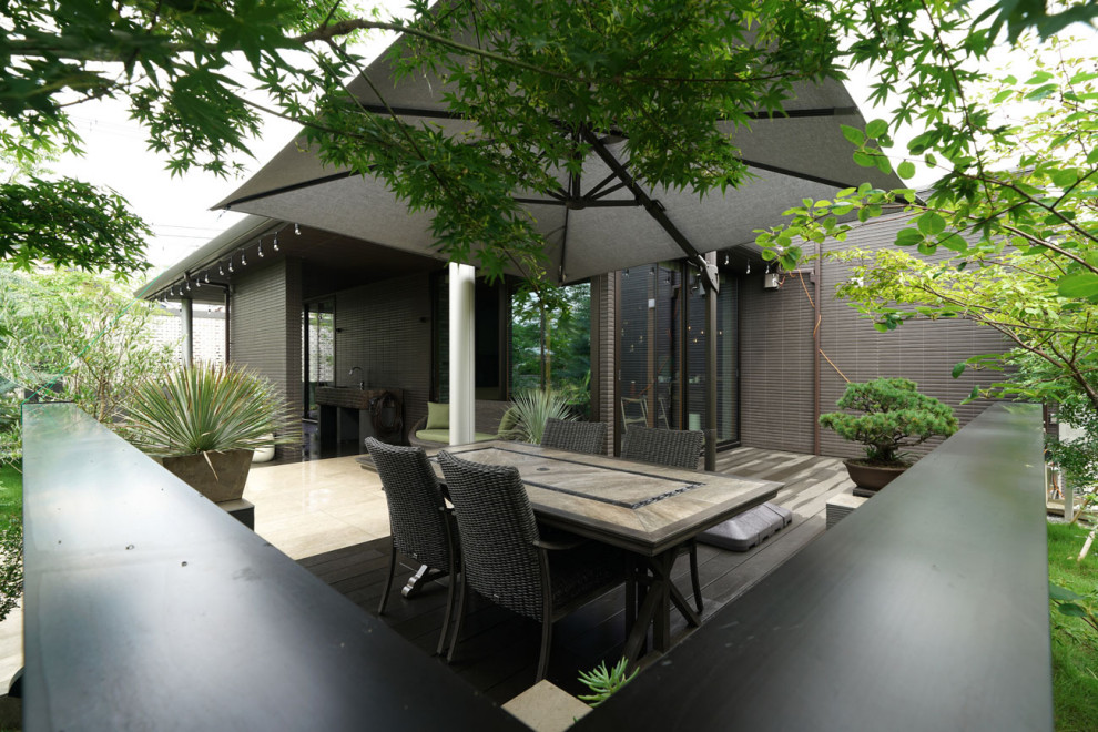 This is an example of an expansive modern side yard and ground level deck in Other with an outdoor kitchen and an awning.