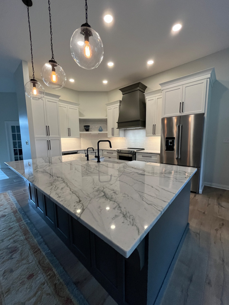 Design ideas for an expansive modern l-shaped eat-in kitchen in Indianapolis with a farmhouse sink, shaker cabinets, quartz benchtops, white splashback, subway tile splashback, stainless steel appliances, vinyl floors, with island, brown floor and white benchtop.