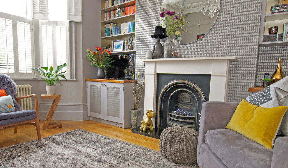 Inspiration for a mid-sized eclectic enclosed living room in London with grey walls, medium hardwood floors, a standard fireplace, a stone fireplace surround, a wall-mounted tv and grey floor.