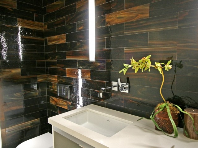 Inspiration for a mid-sized contemporary powder room in Los Angeles with flat-panel cabinets, beige cabinets, a one-piece toilet, brown tile, glass tile, brown walls, an undermount sink and solid surface benchtops.