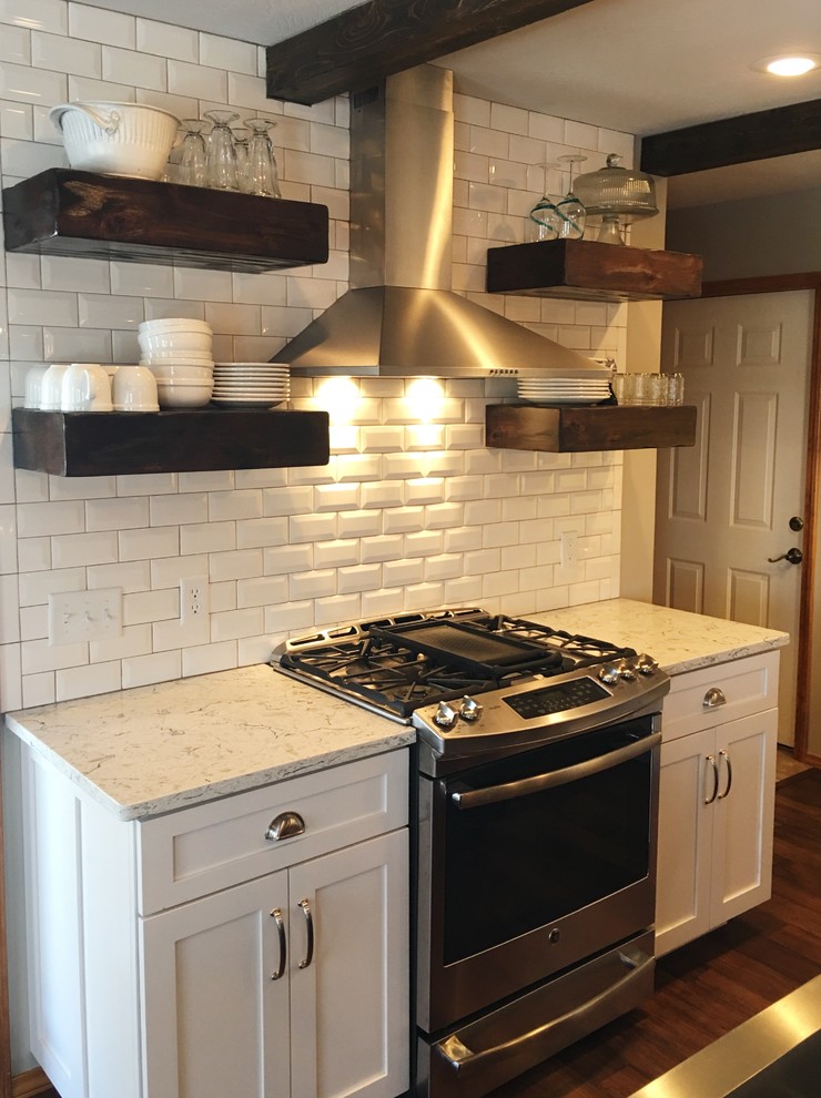 Photo of a large country l-shaped eat-in kitchen in Other with a farmhouse sink, shaker cabinets, white cabinets, quartz benchtops, white splashback, subway tile splashback, stainless steel appliances, dark hardwood floors and with island.