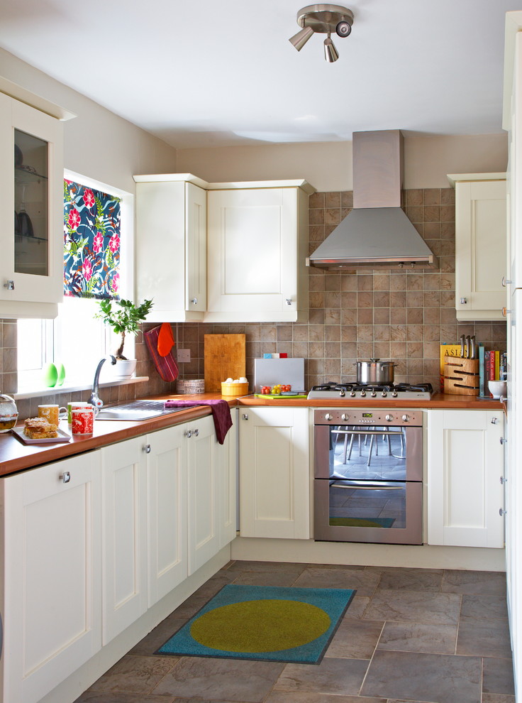 Inspiration for an eclectic separate kitchen in Dublin with a drop-in sink, recessed-panel cabinets, white cabinets, brown splashback, stainless steel appliances and slate splashback.