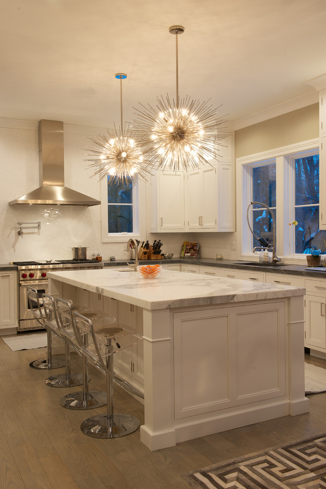 Mid-sized transitional l-shaped open plan kitchen in New York with an undermount sink, recessed-panel cabinets, white cabinets, marble benchtops, white splashback, stainless steel appliances, light hardwood floors, with island and brown floor.
