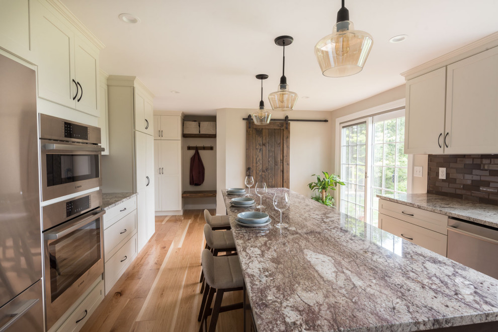 Inspiration for a mid-sized transitional u-shaped light wood floor and brown floor eat-in kitchen remodel in Boston with an undermount sink, shaker cabinets, white cabinets, granite countertops, brown backsplash, glass tile backsplash, stainless steel appliances, an island and multicolored countertops