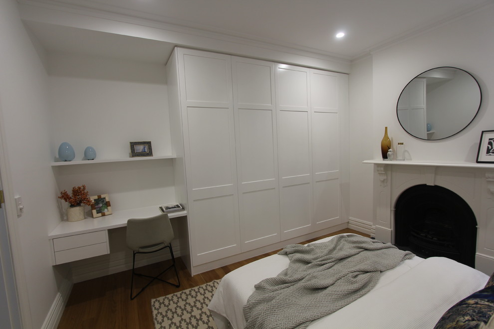 Large transitional guest bedroom in Sydney with white walls, light hardwood floors, a standard fireplace and a wood fireplace surround.