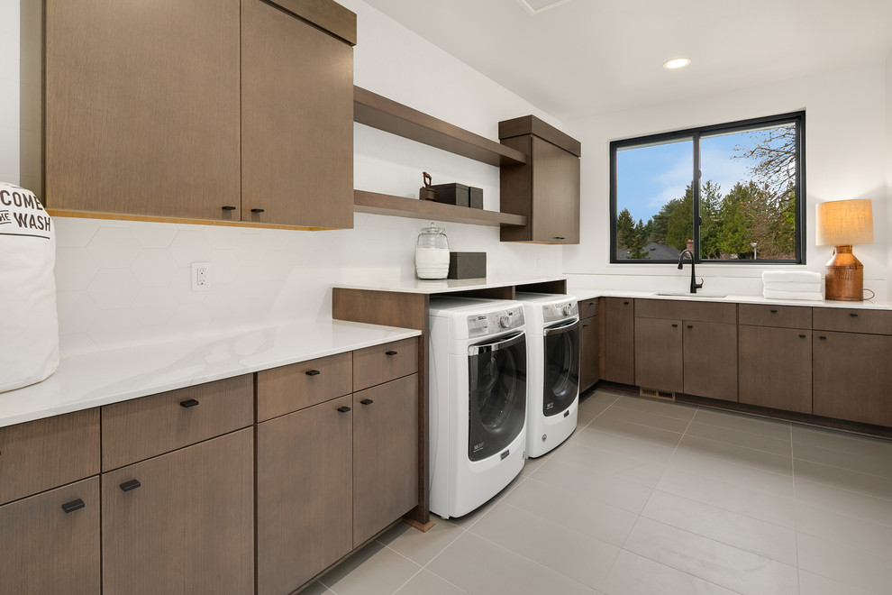 This is an example of a large contemporary l-shaped dedicated laundry room in Seattle with an undermount sink, flat-panel cabinets, quartz benchtops, white walls, a side-by-side washer and dryer, grey floor, white benchtop and medium wood cabinets.