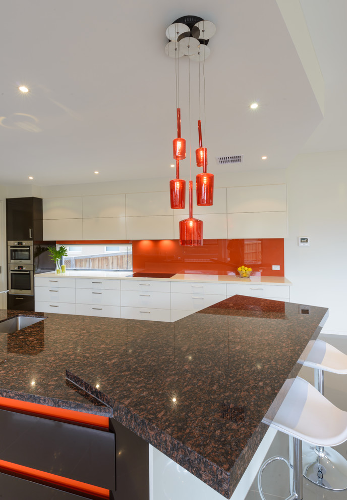 Inspiration for a large contemporary open plan kitchen in Melbourne with an undermount sink, flat-panel cabinets, black cabinets, granite benchtops, glass sheet splashback, stainless steel appliances, porcelain floors, with island and orange splashback.