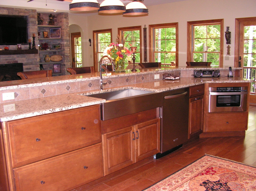 This is an example of a large traditional l-shaped open plan kitchen in Boston with a farmhouse sink, raised-panel cabinets, medium wood cabinets, granite benchtops, beige splashback, ceramic splashback, stainless steel appliances, medium hardwood floors and with island.