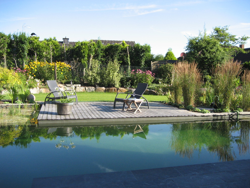Large traditional backyard custom-shaped natural pool in Dortmund with decking.
