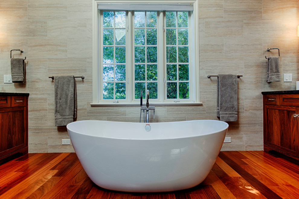 Photo of a large transitional master bathroom in Philadelphia with furniture-like cabinets, dark wood cabinets, a freestanding tub, an open shower, a two-piece toilet, beige tile, porcelain tile, beige walls, medium hardwood floors, an undermount sink and granite benchtops.