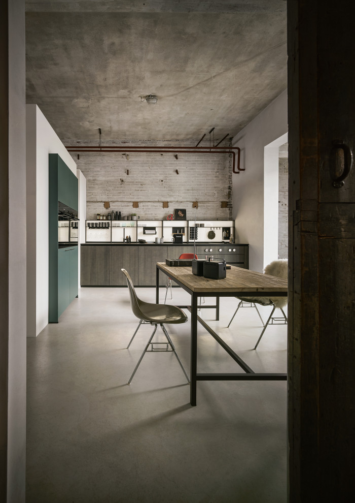 This is an example of an industrial l-shaped open plan kitchen in Nuremberg with flat-panel cabinets, dark wood cabinets, black appliances and no island.