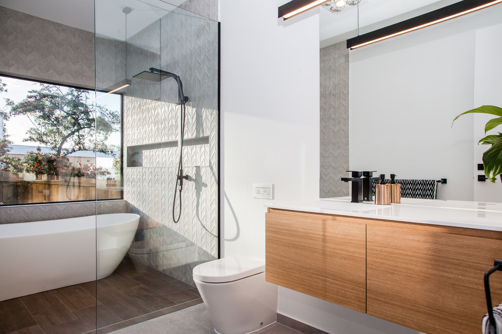 This is an example of a mid-sized contemporary master bathroom in Hobart with flat-panel cabinets, medium wood cabinets, a freestanding tub, an open shower, a wall-mount toilet, gray tile, ceramic tile, white walls, ceramic floors, an integrated sink and laminate benchtops.