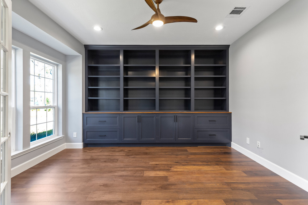 Photo of a mid-sized transitional home office in Houston with a library, grey walls, dark hardwood floors, a standard fireplace, a stone fireplace surround, a built-in desk and brown floor.