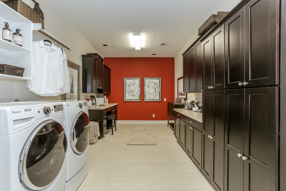 Photo of an expansive transitional u-shaped utility room in Houston with recessed-panel cabinets, black cabinets, solid surface benchtops, red walls, laminate floors, a side-by-side washer and dryer and beige floor.
