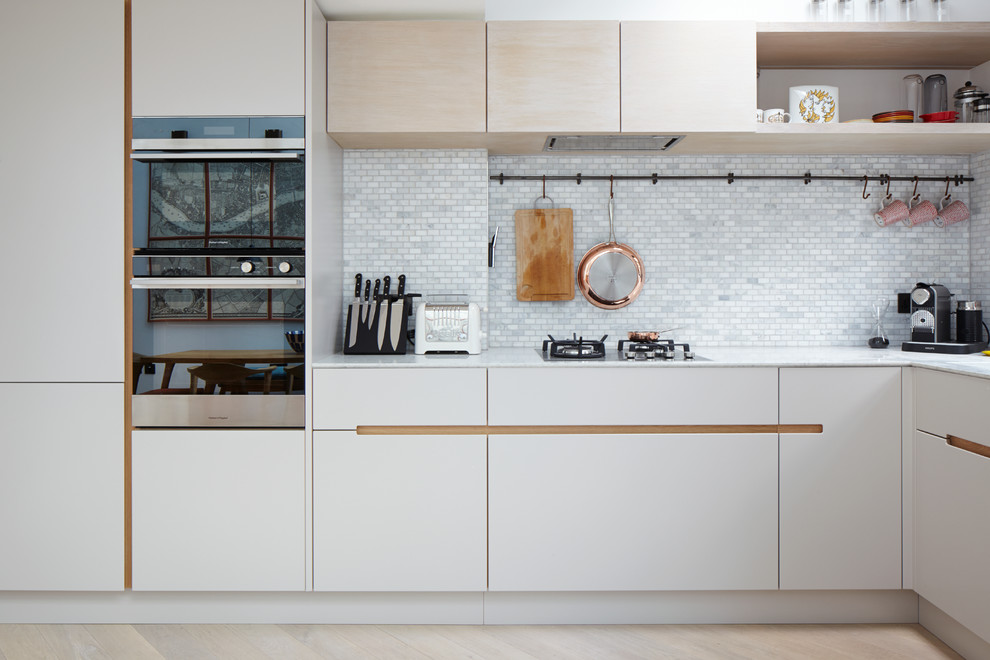 Small contemporary l-shaped eat-in kitchen in London with an integrated sink, flat-panel cabinets, white cabinets, granite benchtops, beige splashback, ceramic splashback, stainless steel appliances, light hardwood floors and no island.