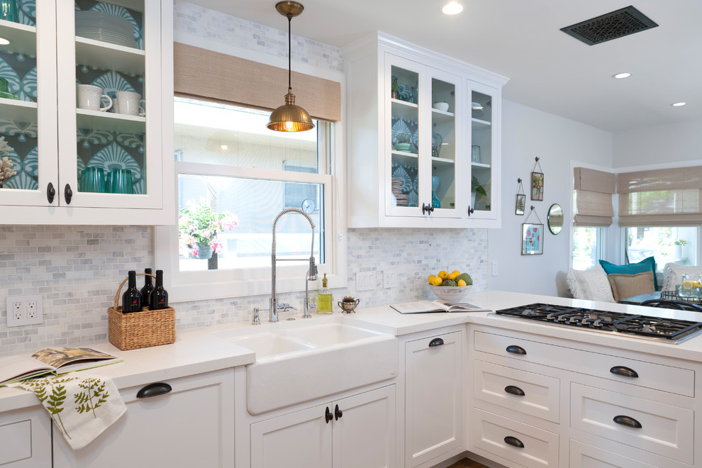 Photo of a beach style l-shaped open plan kitchen in Orange County with shaker cabinets, white cabinets, grey splashback, black appliances, a peninsula and white benchtop.