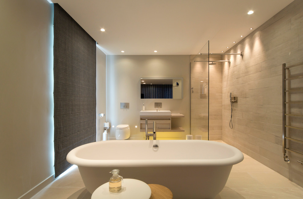 Photo of a contemporary bathroom in London with a freestanding tub, an open shower, a wall-mount toilet, beige tile, white walls, a trough sink and an open shower.