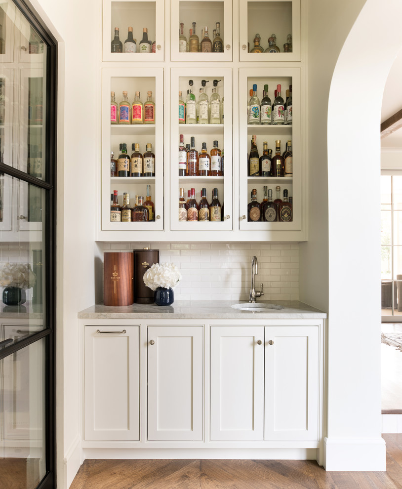 Small transitional single-wall wet bar in Dallas with an undermount sink, beaded inset cabinets, white cabinets, white splashback, medium hardwood floors, brown floor and grey benchtop.