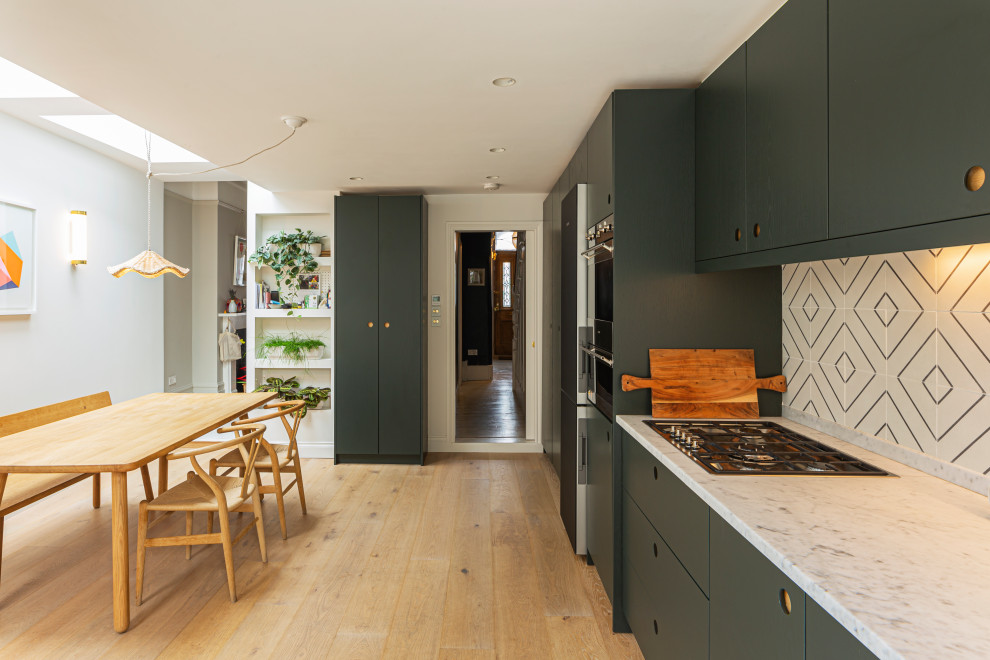 This is an example of a mid-sized contemporary single-wall eat-in kitchen in London with flat-panel cabinets, green cabinets, multi-coloured splashback, black appliances, light hardwood floors, no island, beige floor and white benchtop.