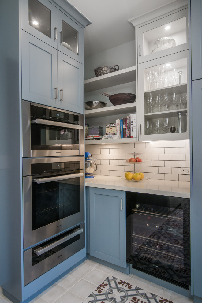 Example of a mid-sized transitional u-shaped ceramic tile and multicolored floor enclosed kitchen design with an undermount sink, shaker cabinets, blue cabinets, limestone countertops, white backsplash, subway tile backsplash, stainless steel appliances, a peninsula and white countertops