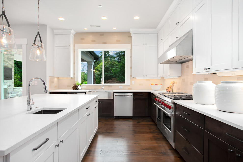 Inspiration for a large arts and crafts l-shaped eat-in kitchen in Seattle with a farmhouse sink, recessed-panel cabinets, white cabinets, quartz benchtops, multi-coloured splashback, glass tile splashback, stainless steel appliances, dark hardwood floors, with island, brown floor and white benchtop.