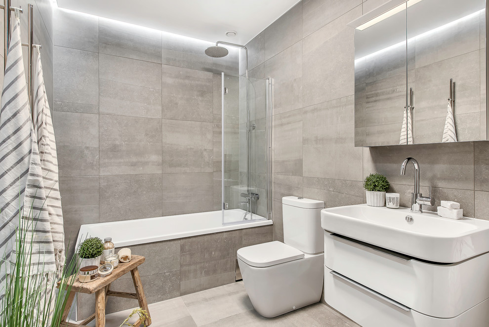 This is an example of a mid-sized modern bathroom in Stockholm with flat-panel cabinets, white cabinets, a shower/bathtub combo, cement tile, a vessel sink, a two-piece toilet, grey walls, limestone floors, a drop-in tub and an open shower.
