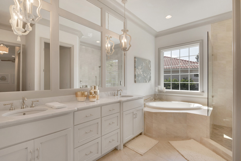 This is an example of a large traditional master bathroom in Miami with recessed-panel cabinets, white walls, an undermount sink, marble benchtops, white cabinets, a corner tub, a corner shower, ceramic floors, beige tile and an open shower.