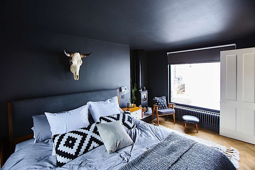 Стильный дизайн: хозяйская спальня среднего размера в стиле фьюжн с черными стенами, светлым паркетным полом, печью-буржуйкой, фасадом камина из камня и бежевым полом - последний тренд