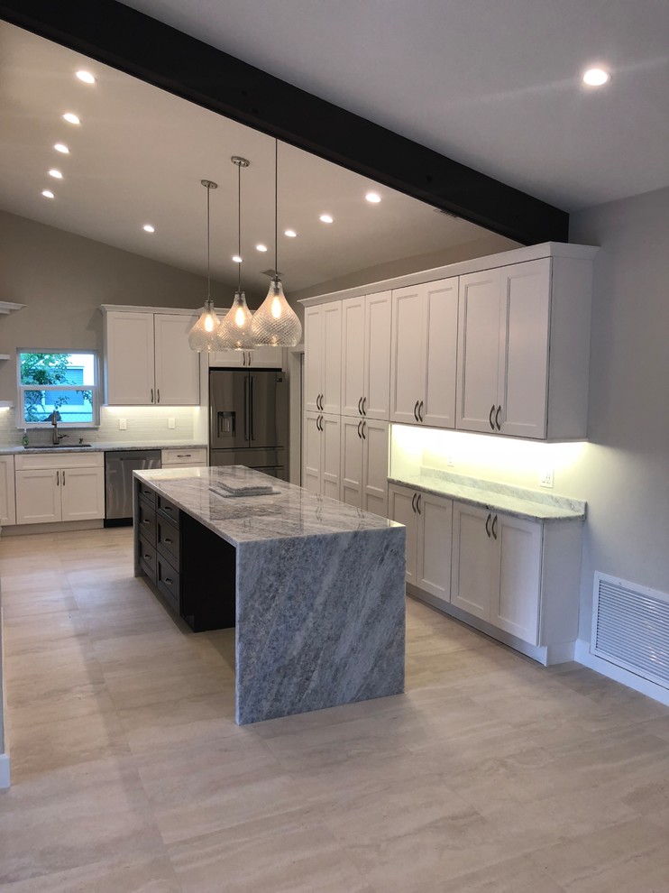 Example of a mid-sized transitional u-shaped beige floor kitchen design in Miami with an undermount sink, recessed-panel cabinets, white cabinets, gray backsplash, glass tile backsplash, stainless steel appliances, an island and gray countertops