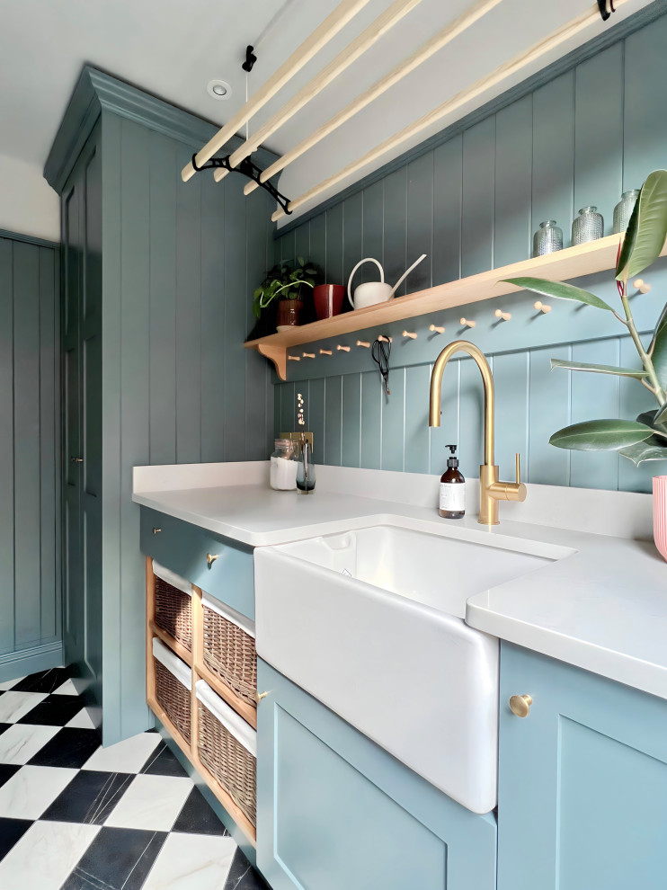 Inspiration for a traditional utility room in Other with a belfast sink, shaker cabinets, blue cabinets, quartz worktops, blue walls, porcelain flooring, a stacked washer and dryer and white worktops.