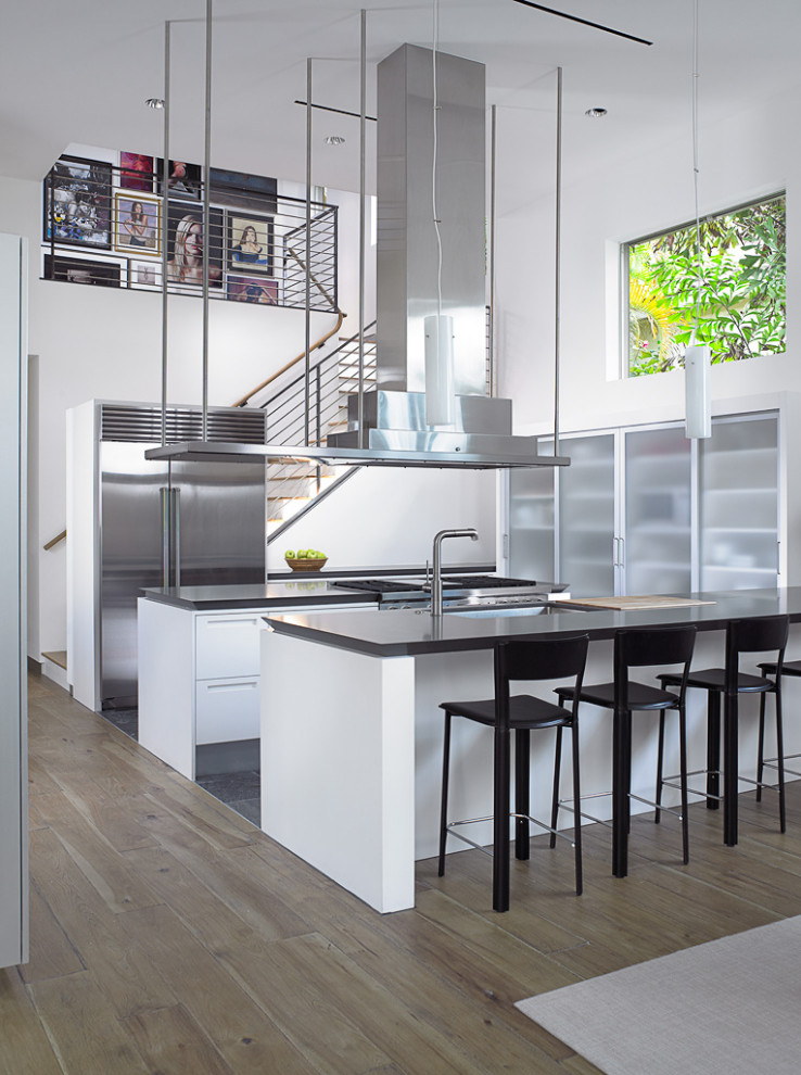 Inspiration for a contemporary u-shaped medium tone wood floor and brown floor open concept kitchen remodel in Miami with an undermount sink, flat-panel cabinets, white cabinets, stainless steel appliances, two islands and black countertops