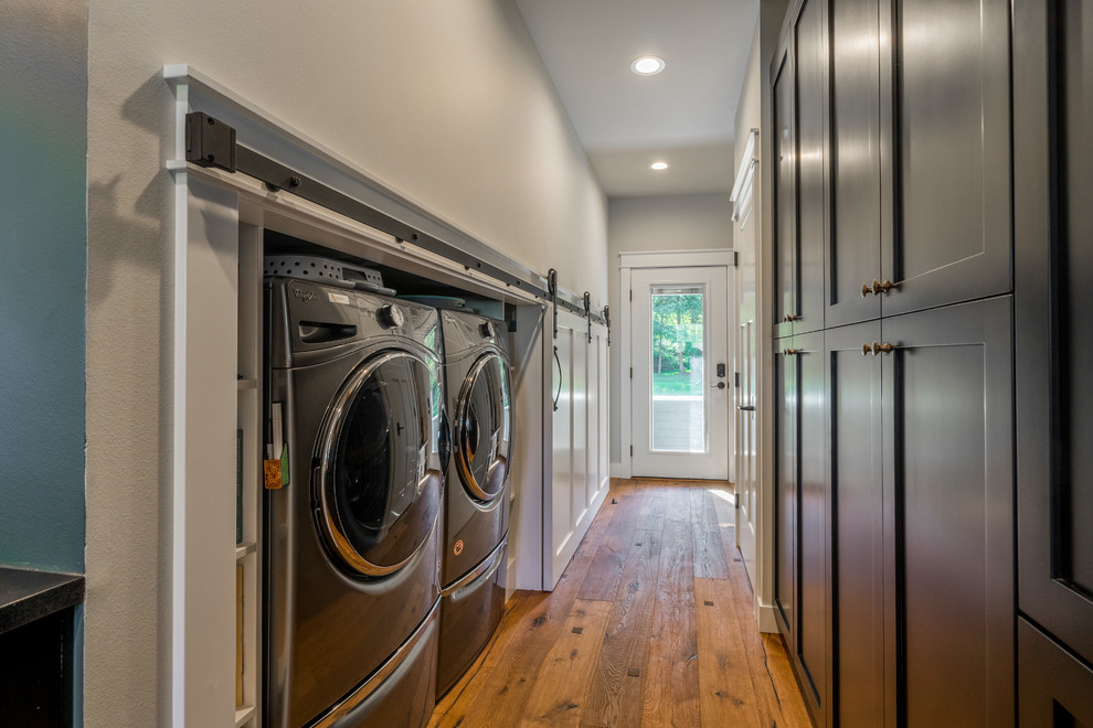 Small country single-wall laundry cupboard in Seattle with shaker cabinets, black cabinets, grey walls, medium hardwood floors, a side-by-side washer and dryer and brown floor.