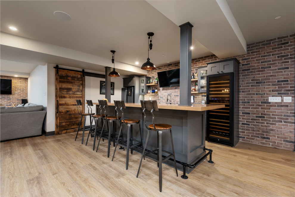 Photo of a large industrial galley seated home bar in Philadelphia with an undermount sink, shaker cabinets, grey cabinets, wood benchtops, multi-coloured splashback, brick splashback, vinyl floors, beige floor and beige benchtop.