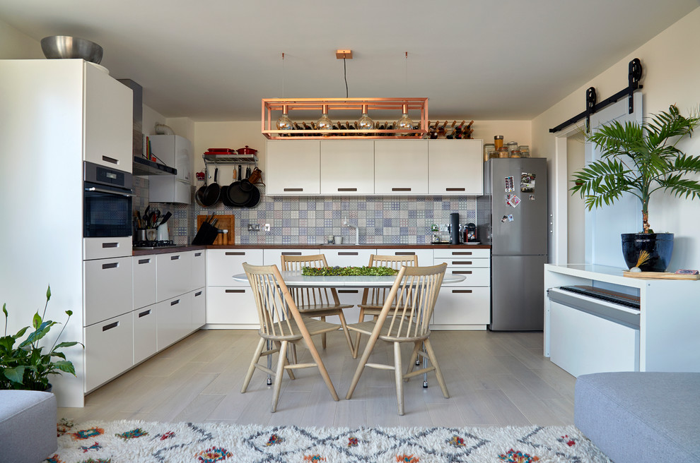 This is an example of a small contemporary l-shaped open plan kitchen in London with flat-panel cabinets, white cabinets, wood benchtops, multi-coloured splashback, ceramic splashback, stainless steel appliances, light hardwood floors, no island, grey floor and brown benchtop.