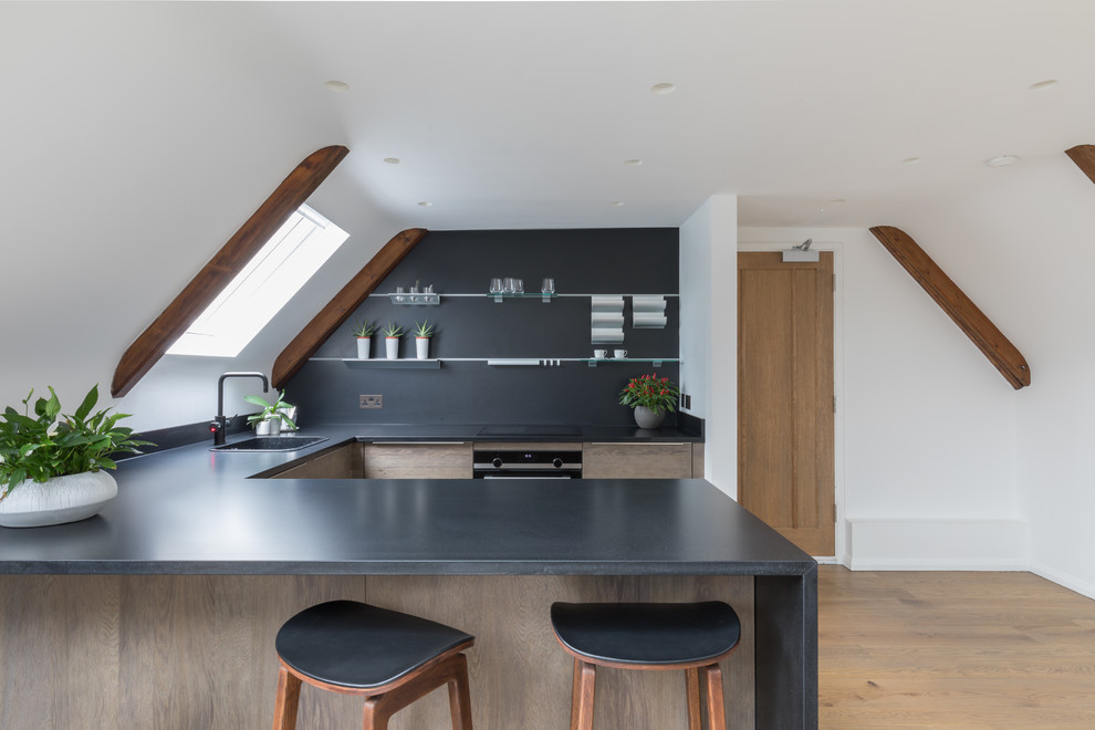 Design ideas for a scandinavian u-shaped kitchen in Sussex with a single-bowl sink, flat-panel cabinets, brown cabinets, black splashback, light hardwood floors, a peninsula and black benchtop.