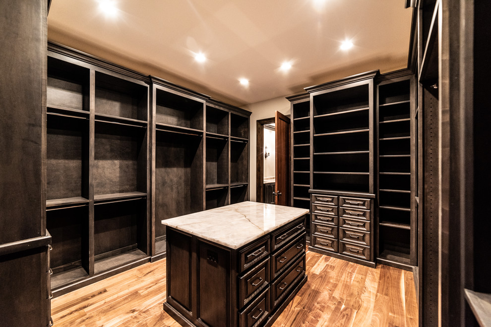 Photo of a mid-sized country gender-neutral walk-in wardrobe in Other with open cabinets, dark wood cabinets, light hardwood floors and brown floor.