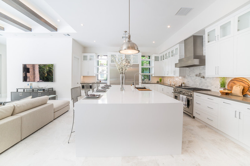 This is an example of an expansive contemporary l-shaped open plan kitchen in Miami with an undermount sink, shaker cabinets, white cabinets, quartzite benchtops, beige splashback, stone tile splashback, stainless steel appliances, porcelain floors, with island, white floor and black benchtop.