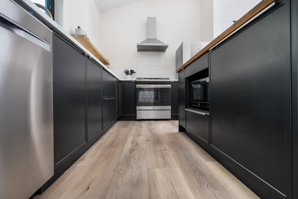 Exempel på ett mellanstort modernt grå grått kök, med en enkel diskho, släta luckor, svarta skåp, marmorbänkskiva, vitt stänkskydd, stänkskydd i keramik, rostfria vitvaror, vinylgolv, en köksö och brunt golv