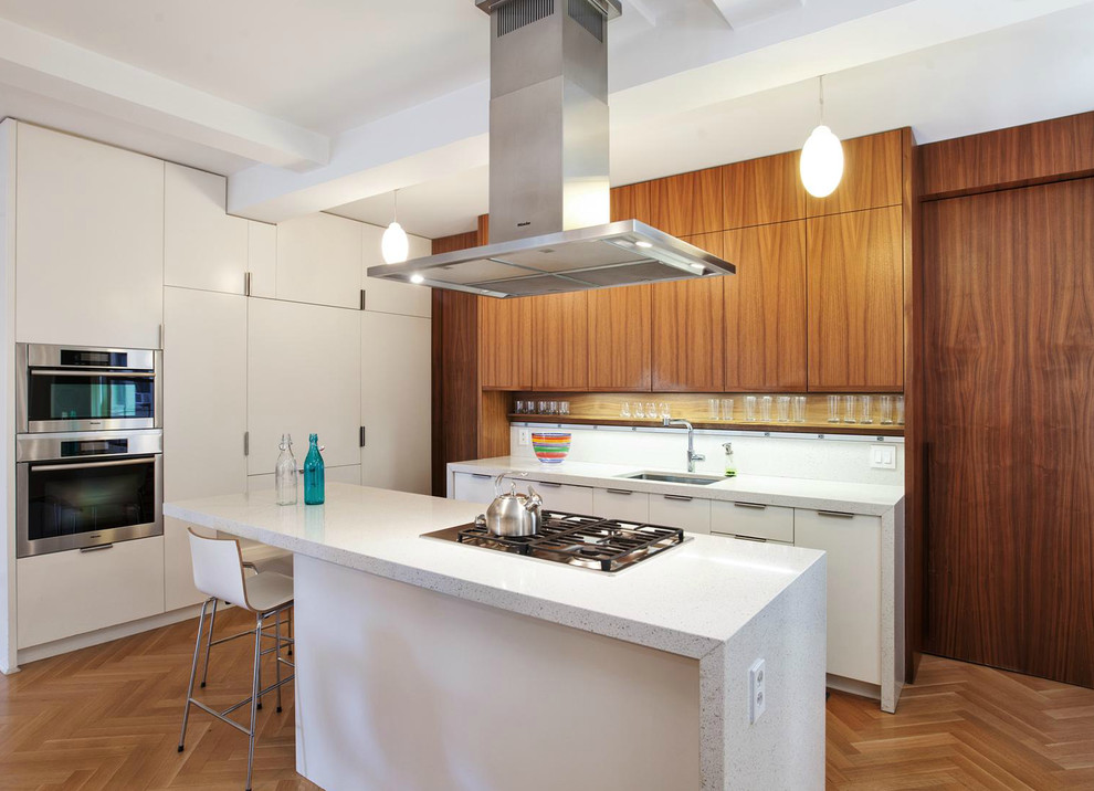 Photo of a contemporary galley kitchen in New York with an undermount sink, flat-panel cabinets, white cabinets, white splashback, stainless steel appliances, medium hardwood floors and with island.