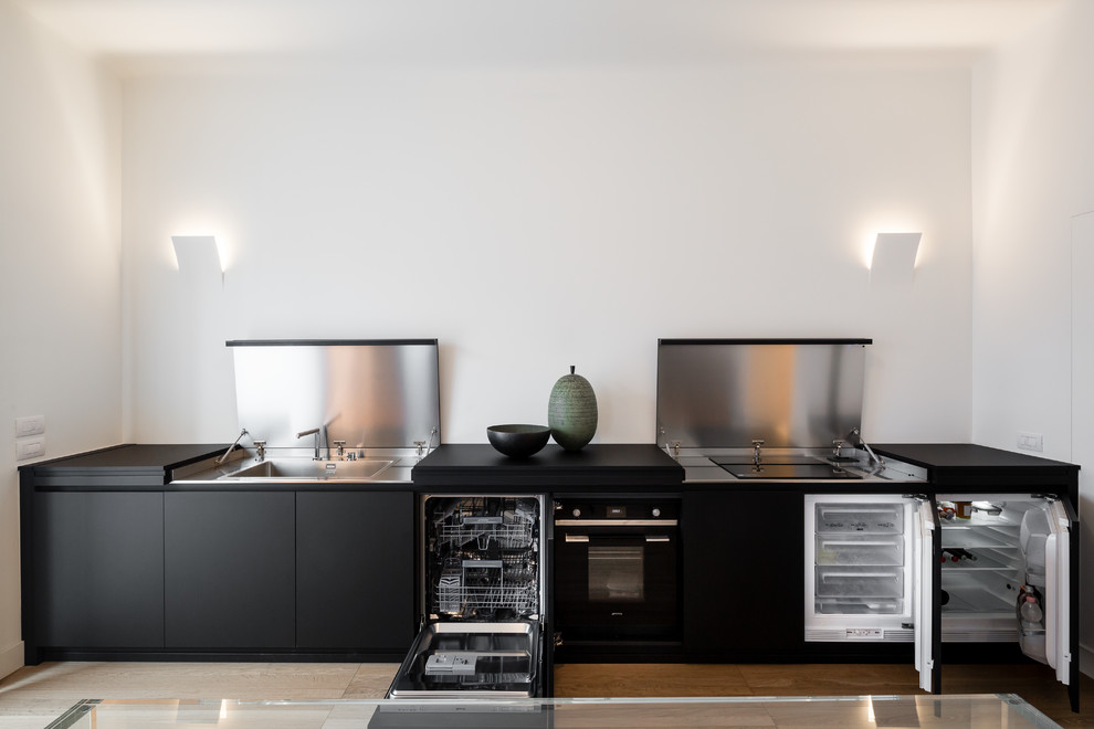 Design ideas for a contemporary single-wall eat-in kitchen in Milan with a single-bowl sink, black cabinets, stainless steel benchtops, stainless steel appliances, light hardwood floors, no island, brown floor and black benchtop.